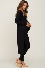 woman wearing a black long sleeve maternity cardigan over a black maternity jumpsuit and holding her baby bump
