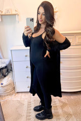 woman wearing a black ribbed maternity dress with a long cardigan and a visible baby bump, posing in front of a mirror