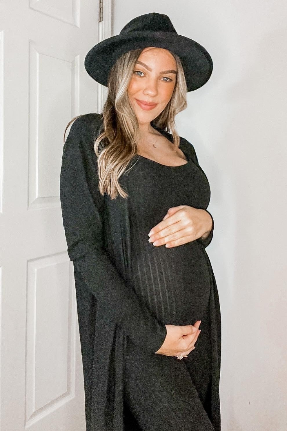 pregnant woman in black maternity dress and fedora hat holding her baby bump