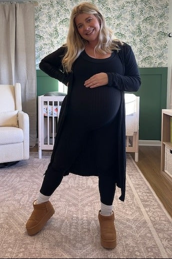 woman wearing a black ribbed maternity outfit with a long cardigan, showing off her baby bump in a cozy setting
