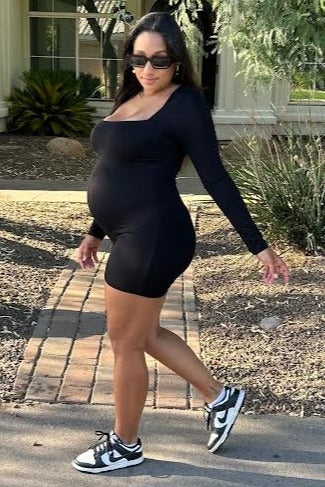 woman wearing a black long sleeve maternity dress with a visible baby bump, paired with black and white sneakers