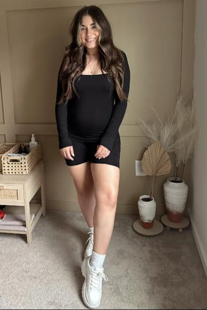 woman wearing a black long sleeve maternity dress with a visible baby bump and white sneakers