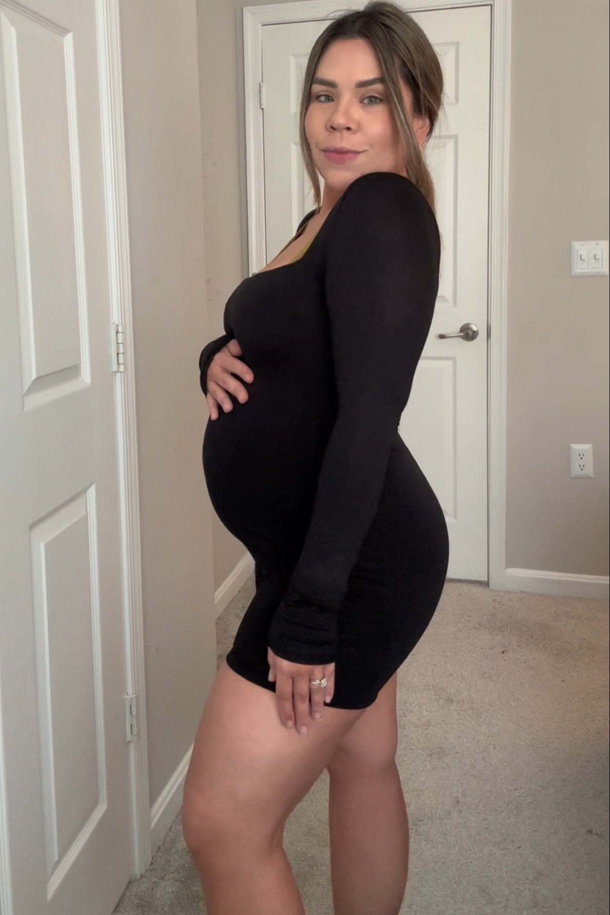 woman wearing a black long sleeve maternity dress and holding her baby bump
