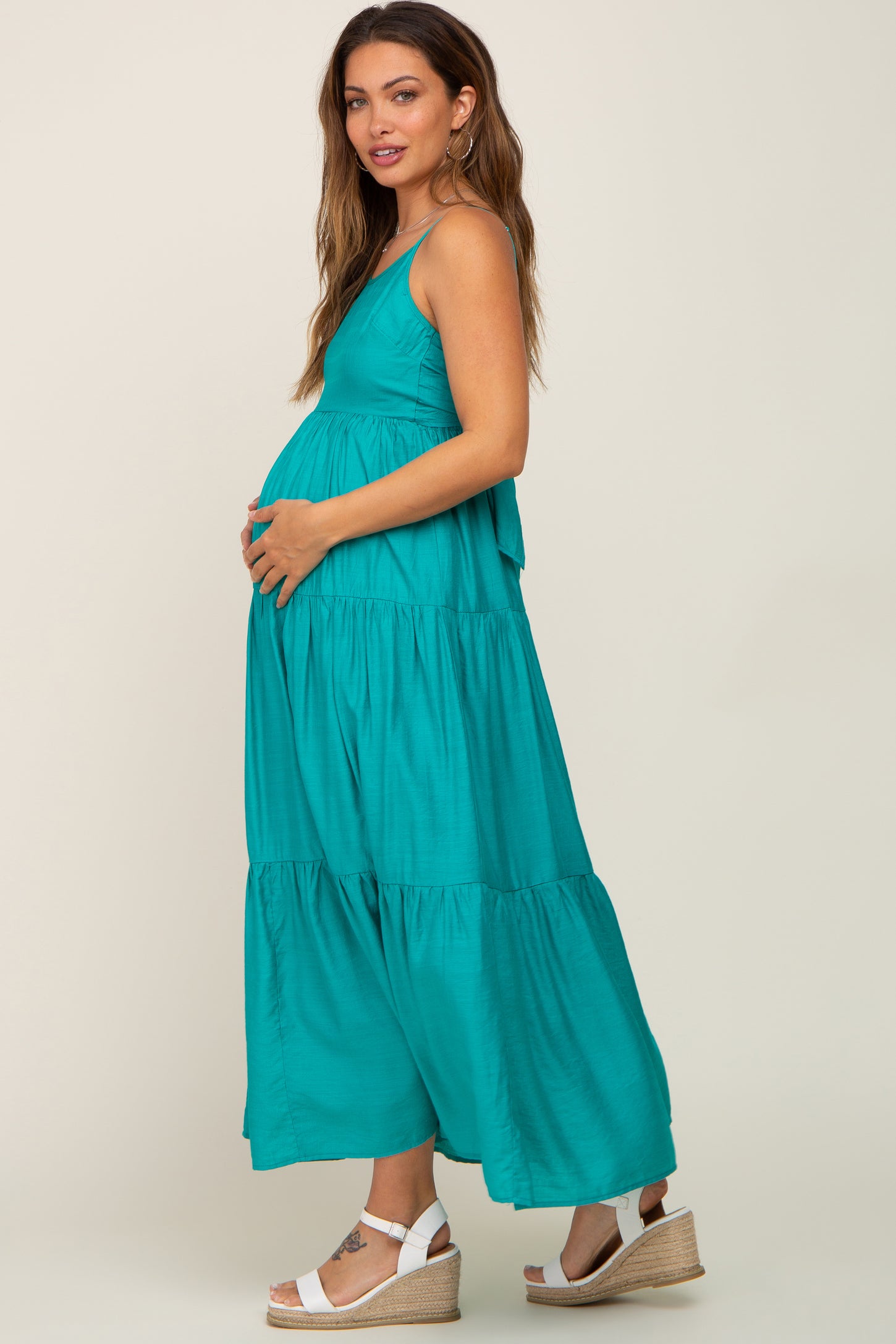 woman wearing a teal maternity maxi dress with tiered layers, holding her baby bump