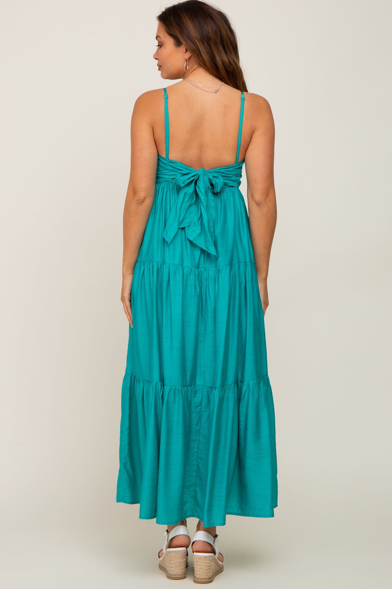 woman wearing a teal maternity maxi dress with a tied bow back detail and tiered skirt