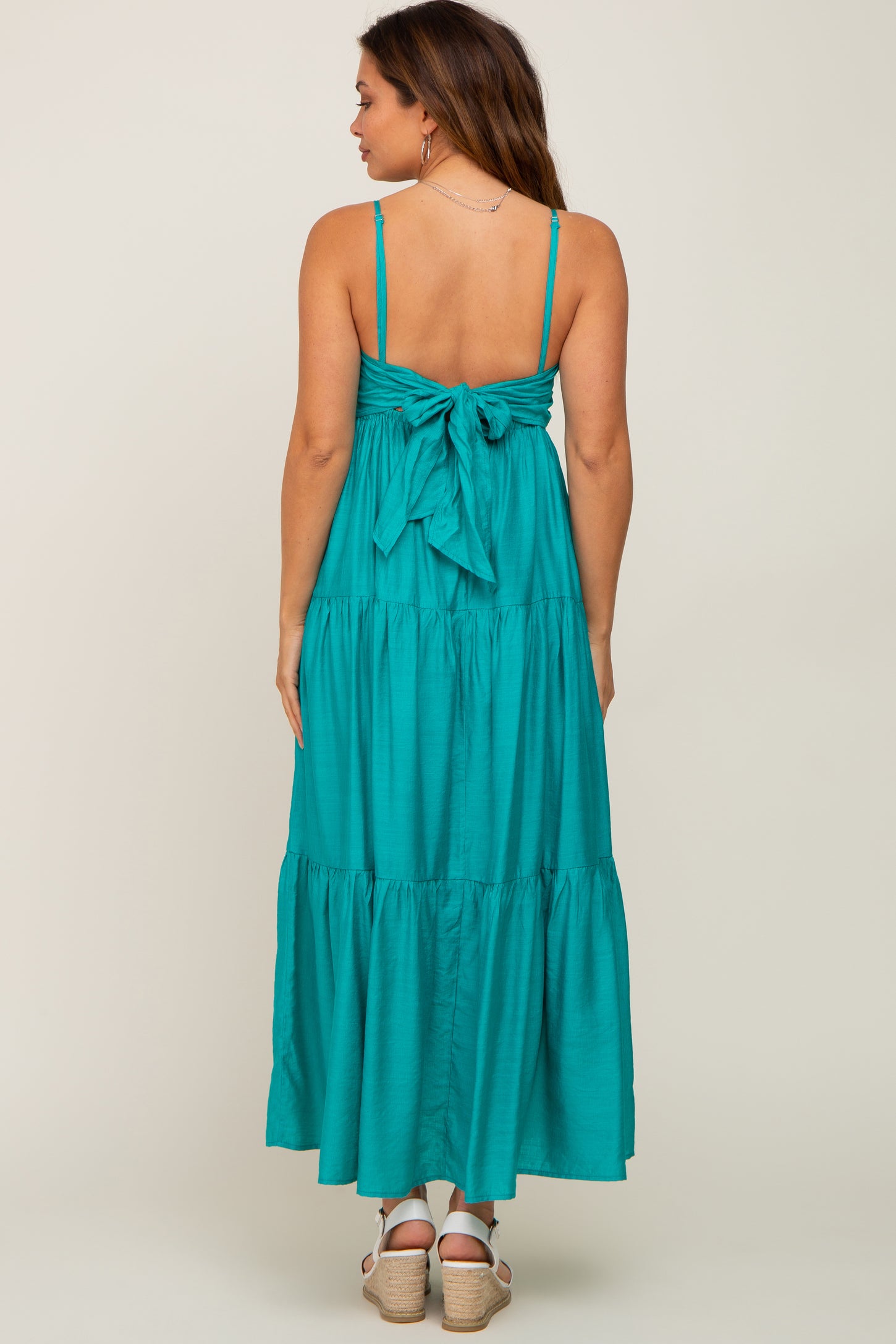 woman wearing a teal maternity maxi dress with a tied bow back detail and tiered skirt