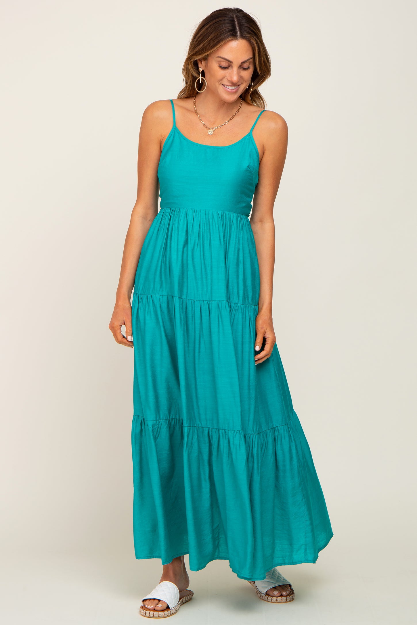 woman wearing a teal maxi dress with adjustable straps and tiered ruffle details