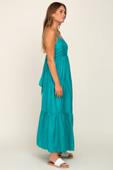 woman wearing a teal maxi dress with a tiered design and spaghetti straps, standing sideways with a relaxed pose
