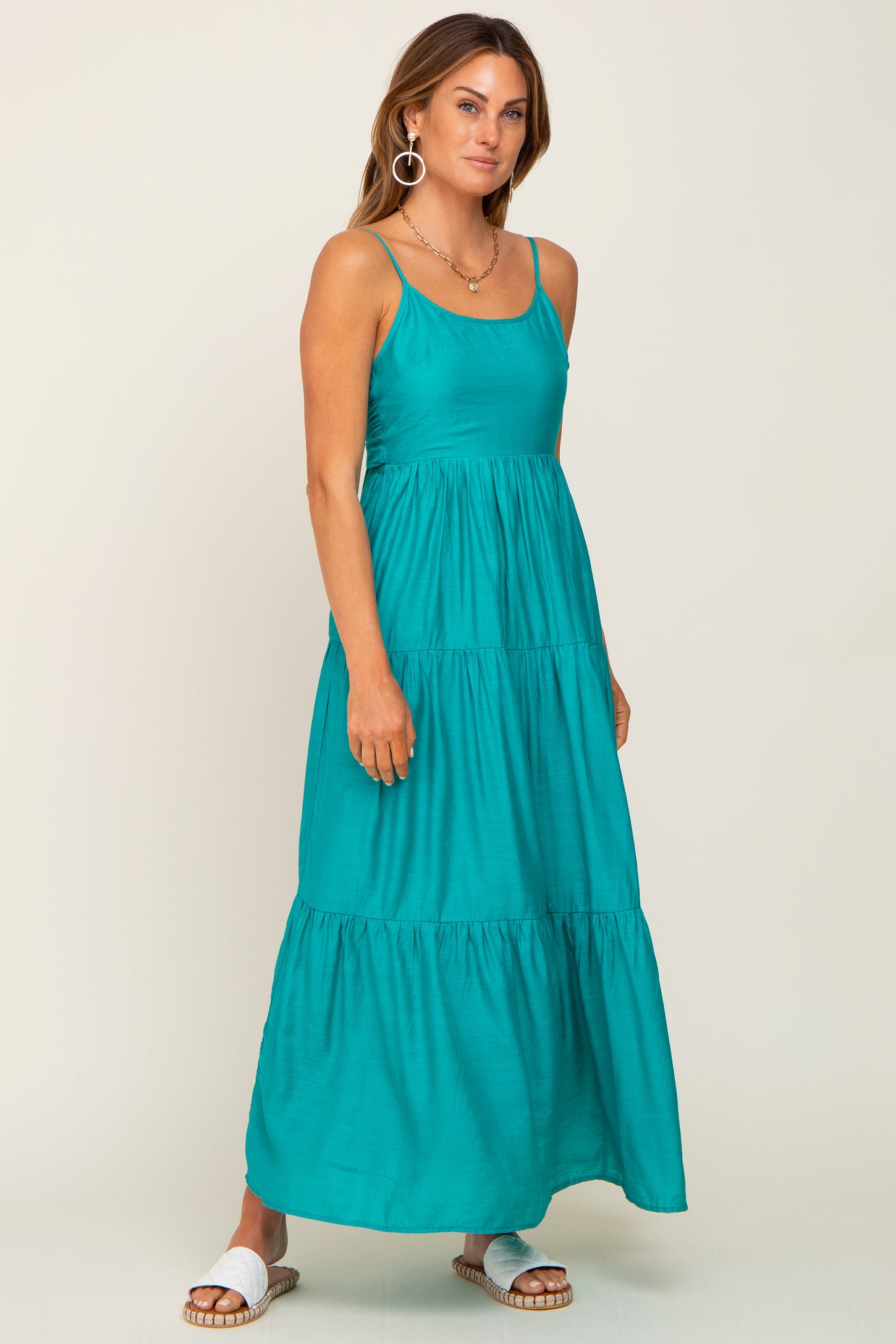 Woman wearing a teal tiered maxi dress with spaghetti straps and white slide sandals