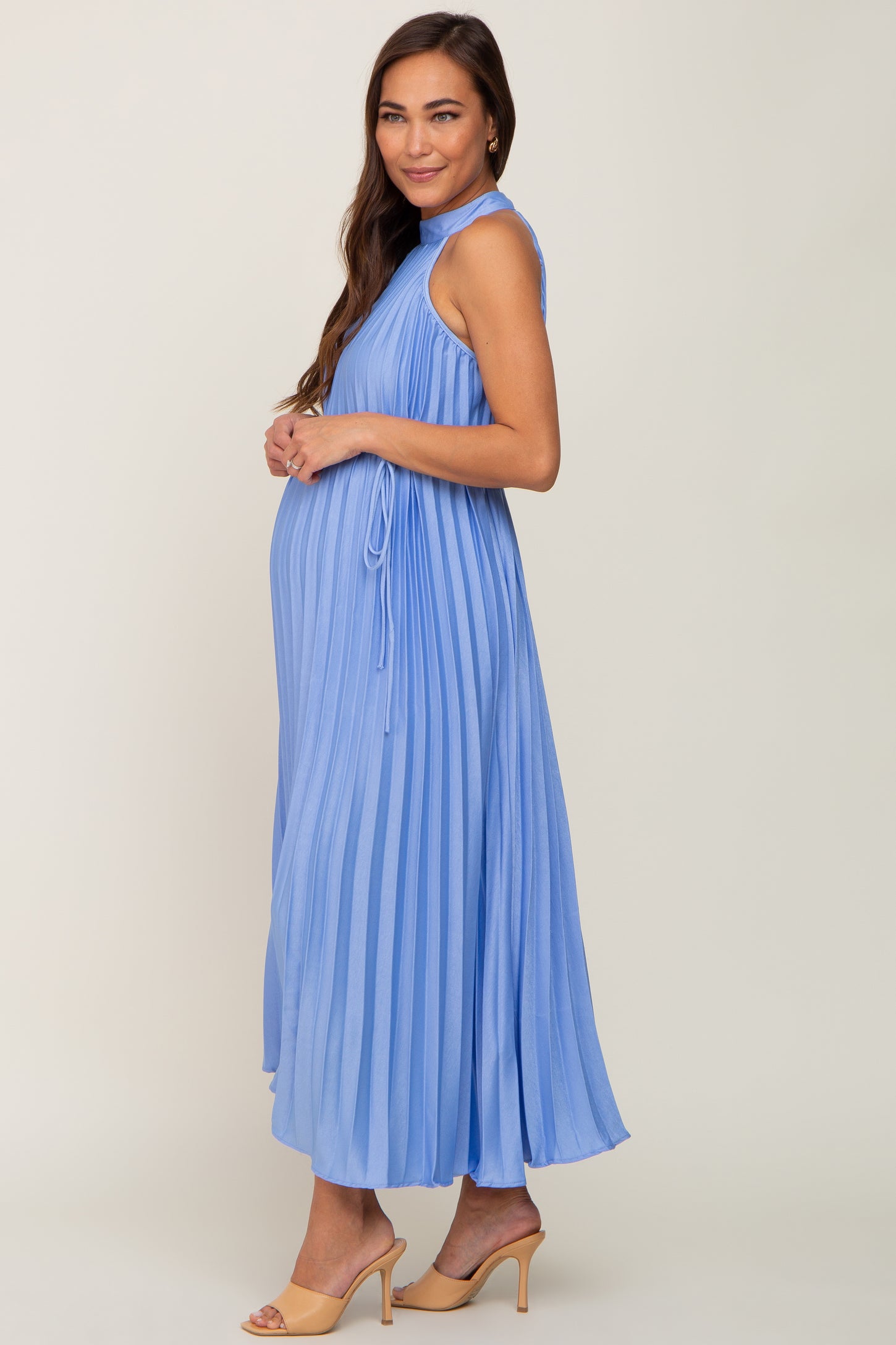 woman wearing a light blue pleated maternity dress showcasing her baby bump