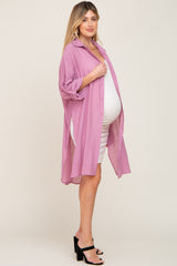 Pregnant woman wearing a mauve oversized button-down shirt over a white maternity dress and black heels