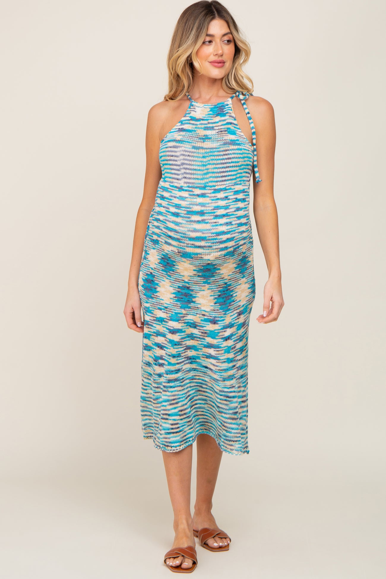 woman wearing a multicolored striped maternity dress with a halter neckline and tie details, showcasing her baby bump