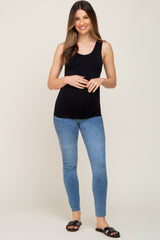 woman wearing a black maternity tank top and skinny jeans, gently holding her baby bump