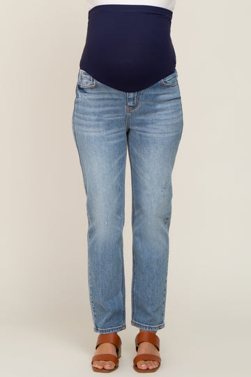 woman wearing light blue maternity jeans with a navy belly band, standing in sandals, showing a baby bump