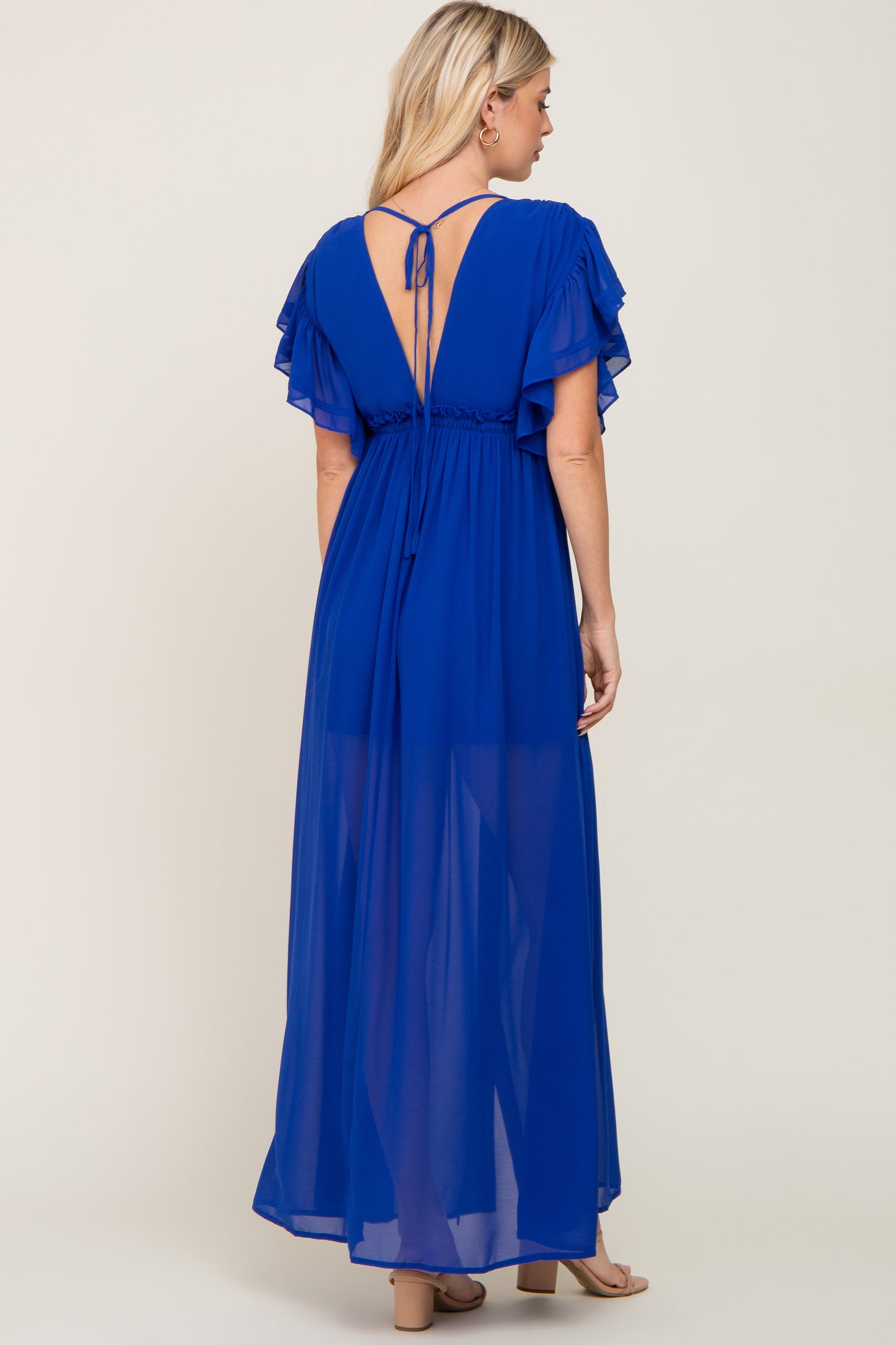 woman wearing a blue maxi dress with ruffled sleeves and an open back, viewed from the back