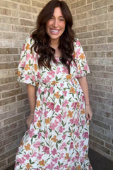 woman wearing a floral print maternity maxi dress with puff sleeves and a tiered hem, smiling in front of a brick wall