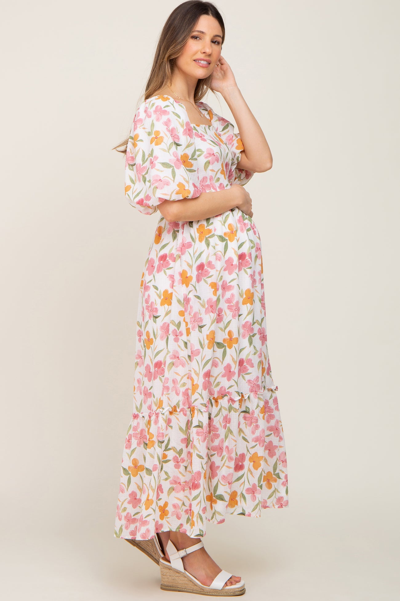 woman wearing a floral maternity maxi dress with puff sleeves and a tiered skirt, holding her baby bump