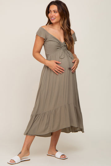 woman wearing a sage green off-shoulder maternity dress with a knotted bodice and a flowing skirt, highlighting her baby bump