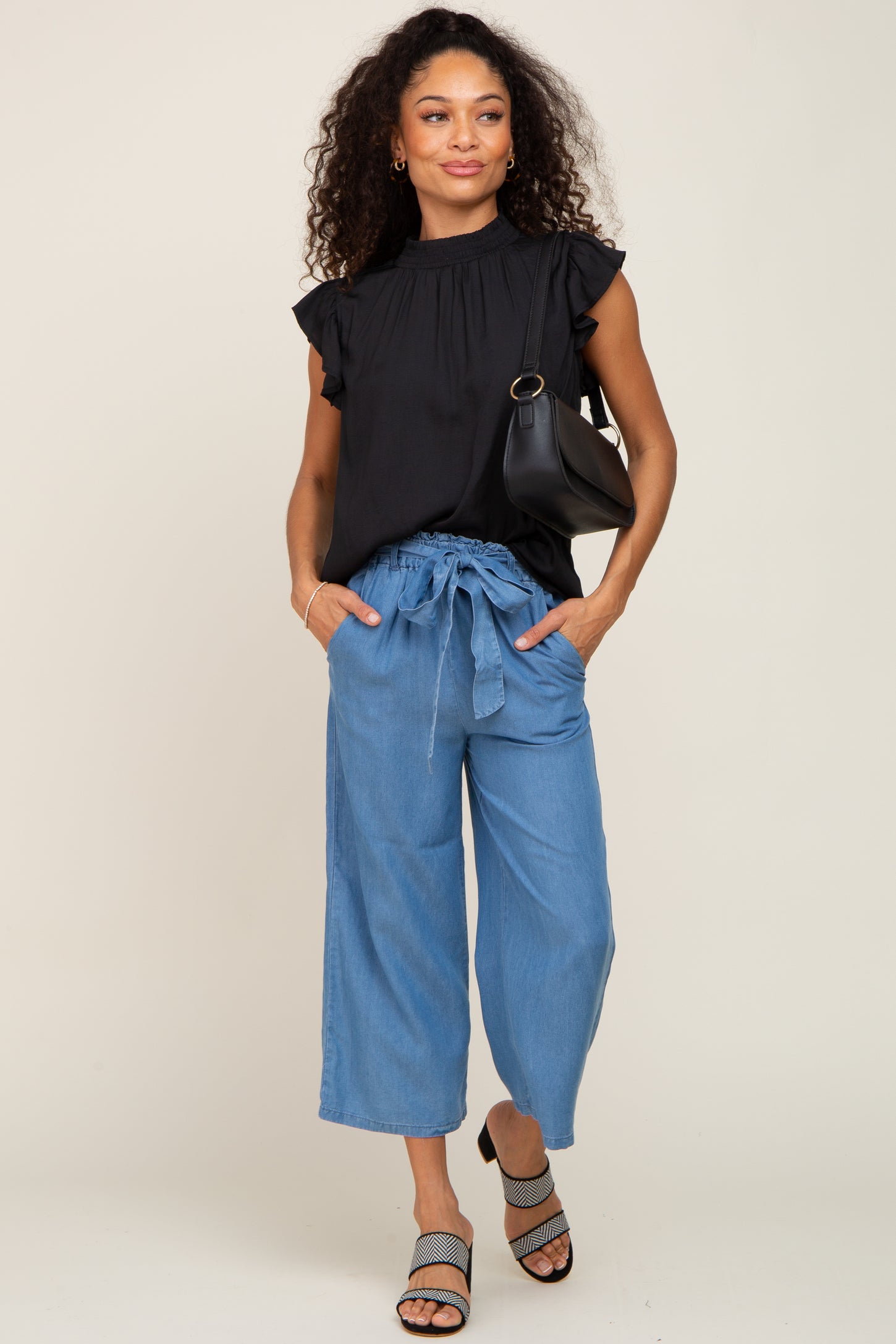 Woman wearing black ruffle sleeve top and blue wide leg tie-waist pants with black shoulder bag