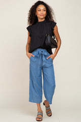 Woman wearing black ruffle sleeve top and blue wide leg tie-waist pants with black shoulder bag