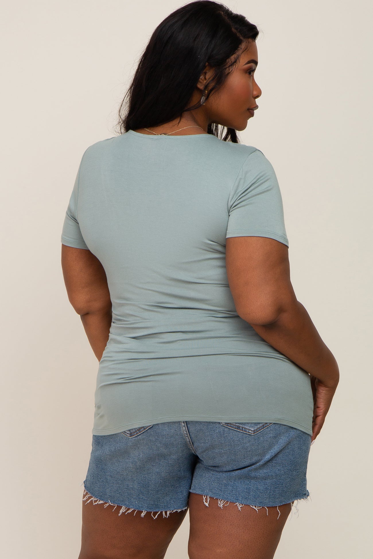 back view of a woman wearing a sage green short sleeve t-shirt and denim shorts