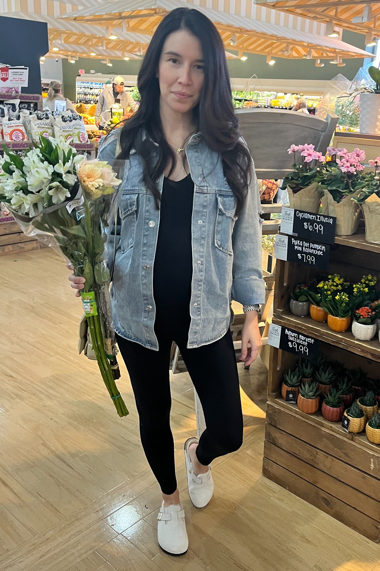 woman in denim jacket and black leggings holding a bouquet of flowers in a grocery store floral department