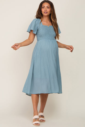 woman wearing a light blue maternity dress with short flutter sleeves and a square neckline, showcasing her baby bump
