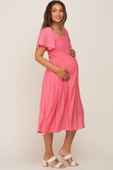 woman wearing a pink maternity dress with flutter sleeves and a smocked bodice, showing her baby bump