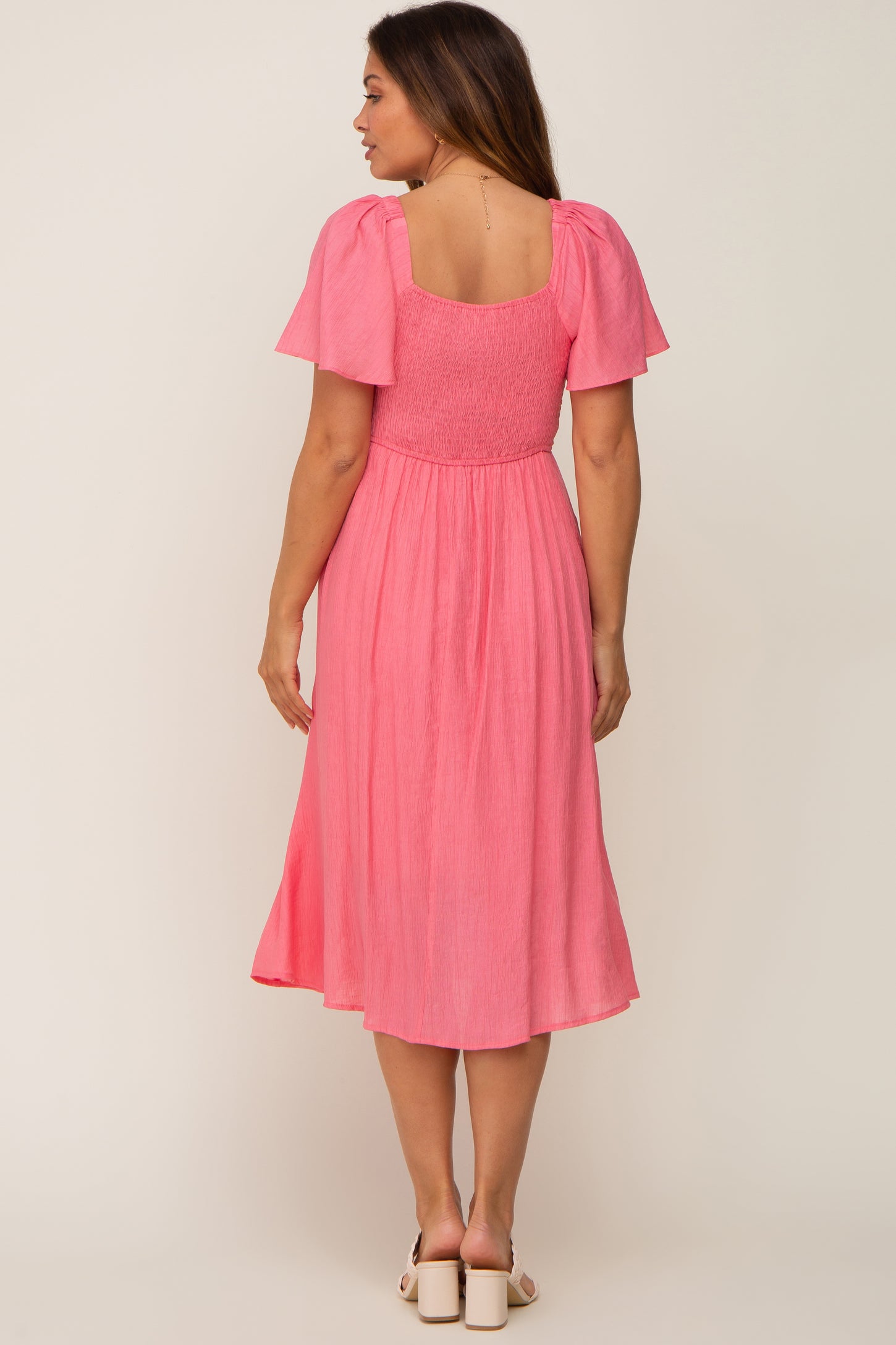 woman wearing a pink maternity dress with short puff sleeves and a smocked bodice, showing a baby bump