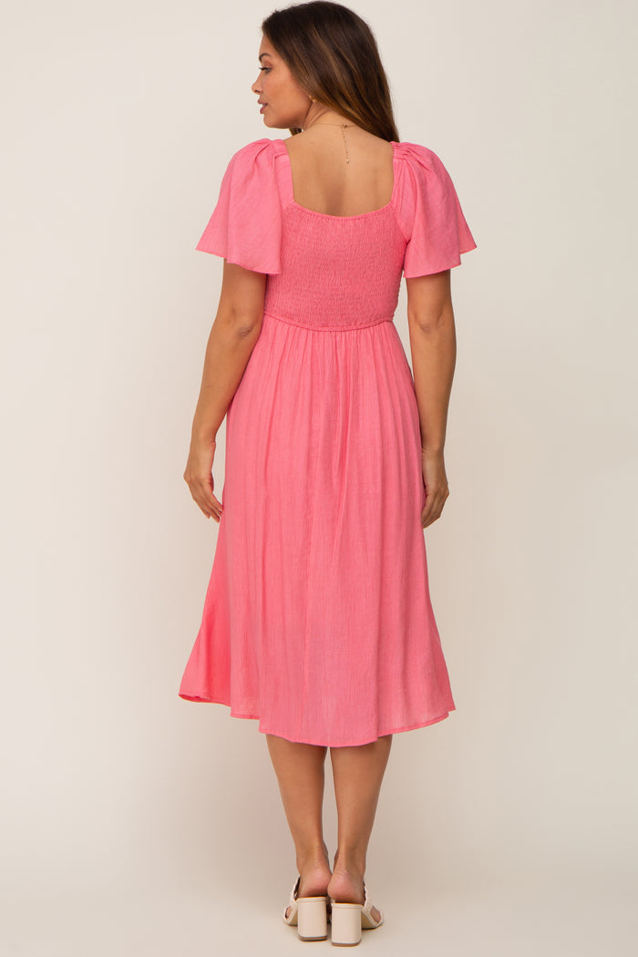 woman wearing a pink maternity dress with short puff sleeves and a smocked bodice, showing a baby bump