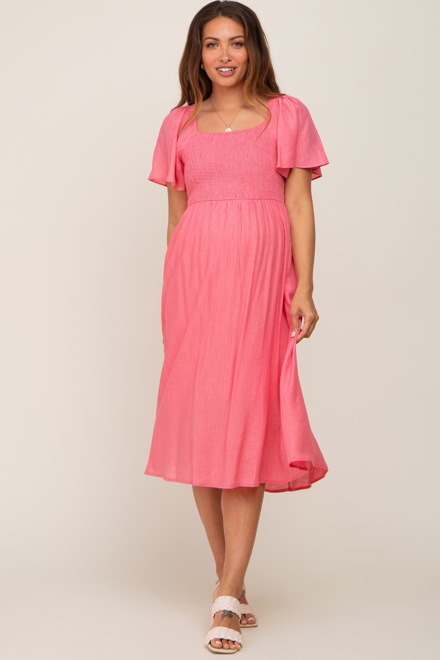 woman wearing a pink maternity dress with short puff sleeves and a smocked bodice, showcasing her baby bump