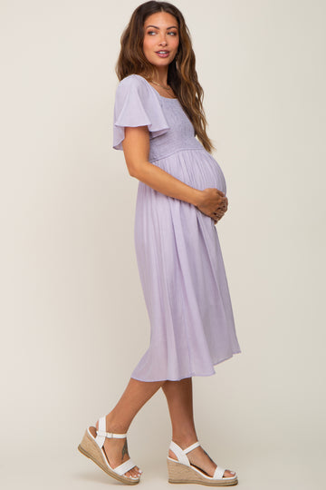 woman wearing a lavender maternity dress with flutter sleeves and a visible baby bump