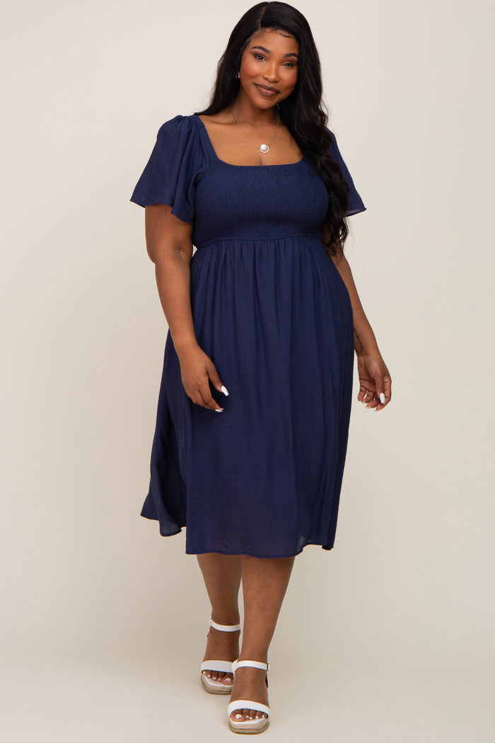 plus size woman wearing a navy blue smocked midi dress with flutter sleeves and white sandals