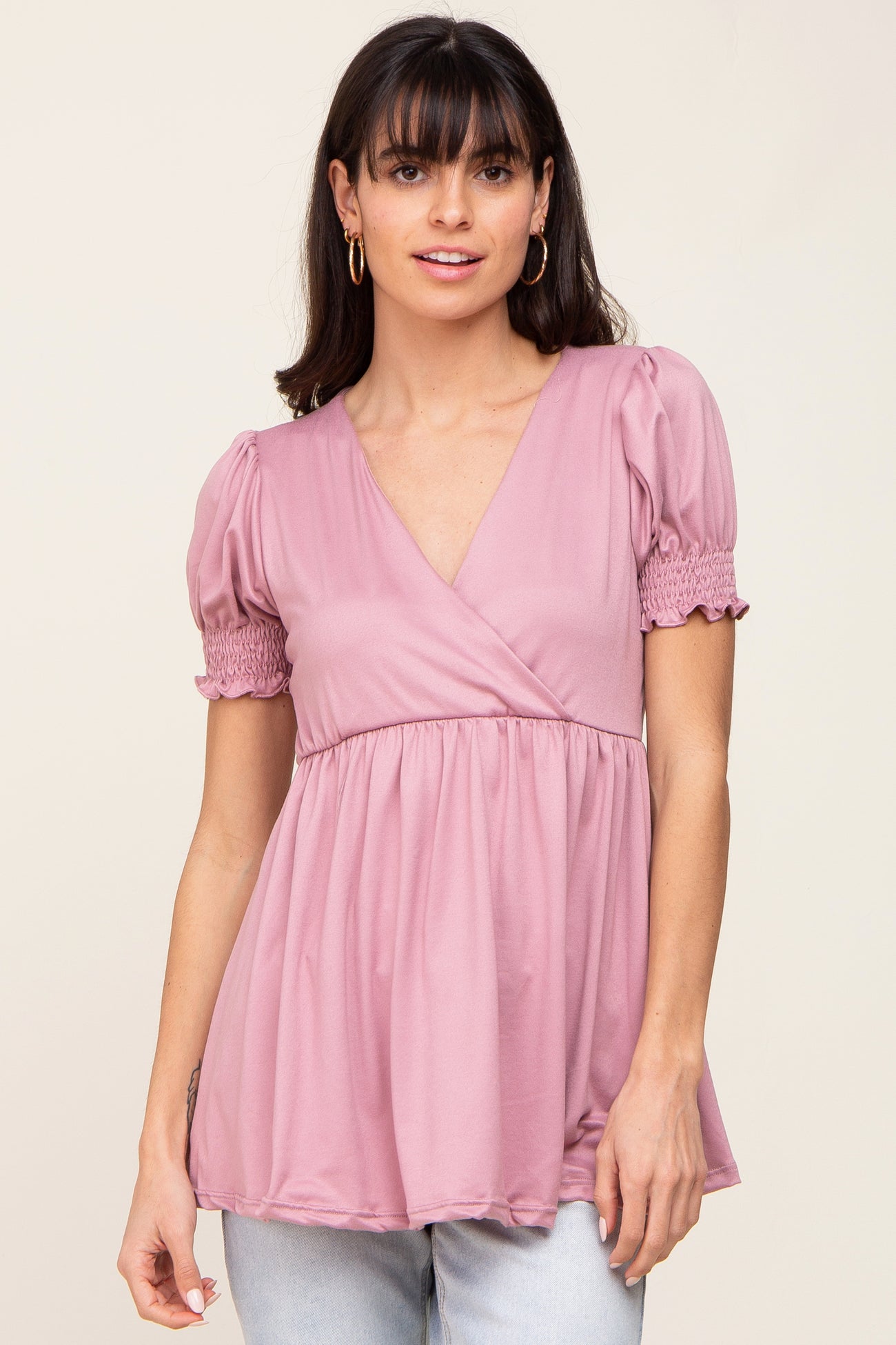 woman wearing a pink v-neck top with puff sleeves and gathered details, styled with light blue jeans