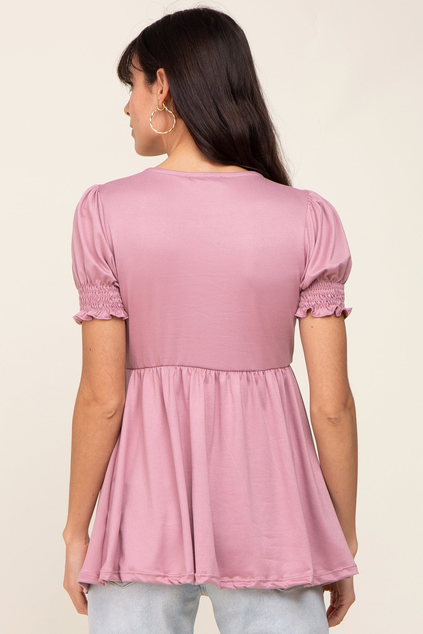 woman wearing a pink puff sleeve top with a smocked waist and flowy hem, showing the back view