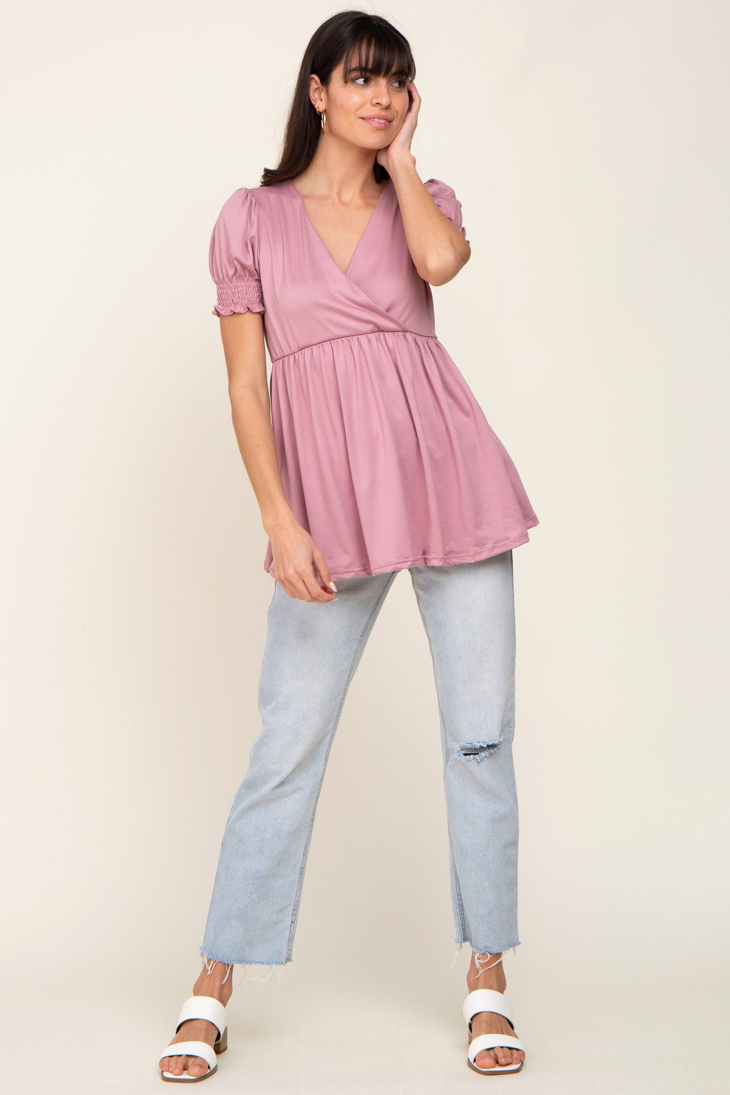 woman wearing a light pink short sleeve peplum top with a v-neck and relaxed fit, paired with light blue distressed jeans
