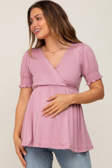 woman wearing a light pink maternity wrap top with smocked sleeves and holding her baby bump