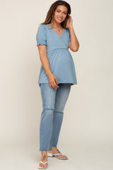 woman wearing a light blue maternity top with short puff sleeves and a baby bump, paired with distressed light wash jeans