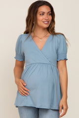 woman wearing a light blue maternity top with a v-neck and puff sleeves, highlighting her baby bump