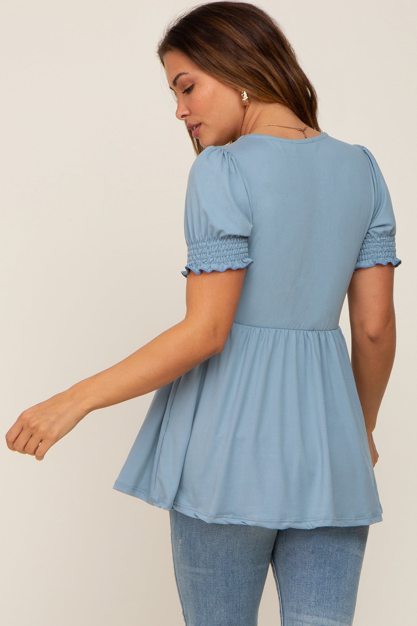 woman wearing a light blue maternity top with puff sleeves and a smocked waist, showing the back view