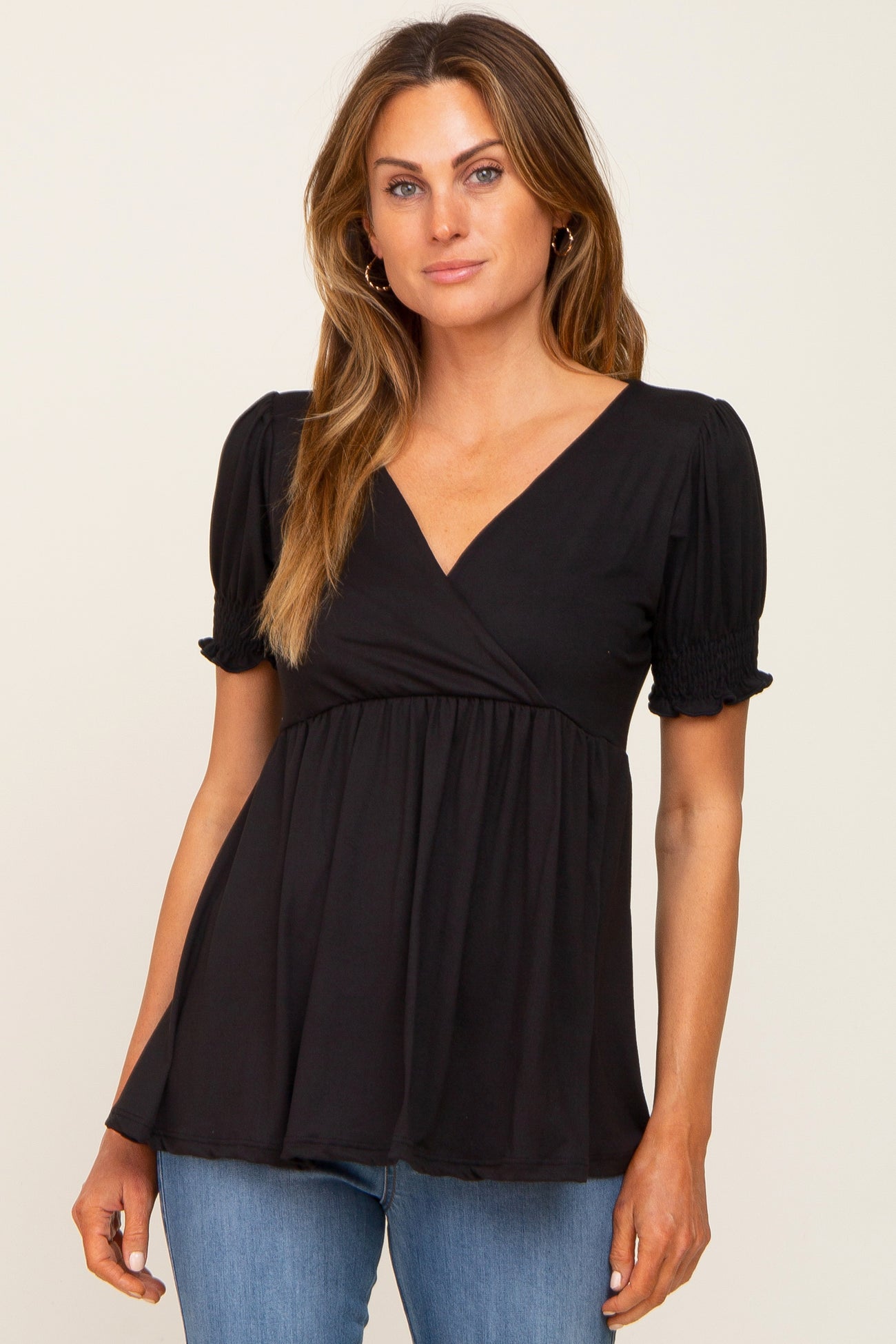 woman wearing a black short sleeve wrap top with smocked details and a flowy fit, paired with blue jeans