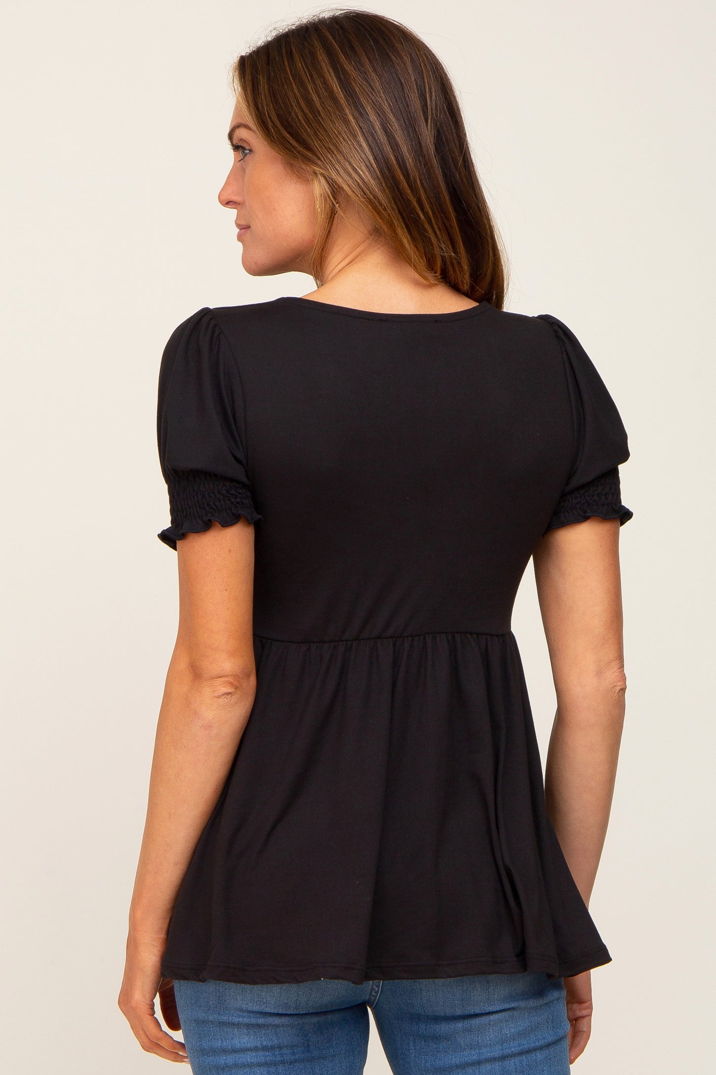 woman wearing a black short sleeve top with puffed sleeves and a peplum waist, viewed from the back