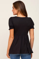 woman wearing a black short sleeve top with puffed sleeves and a peplum waist, viewed from the back