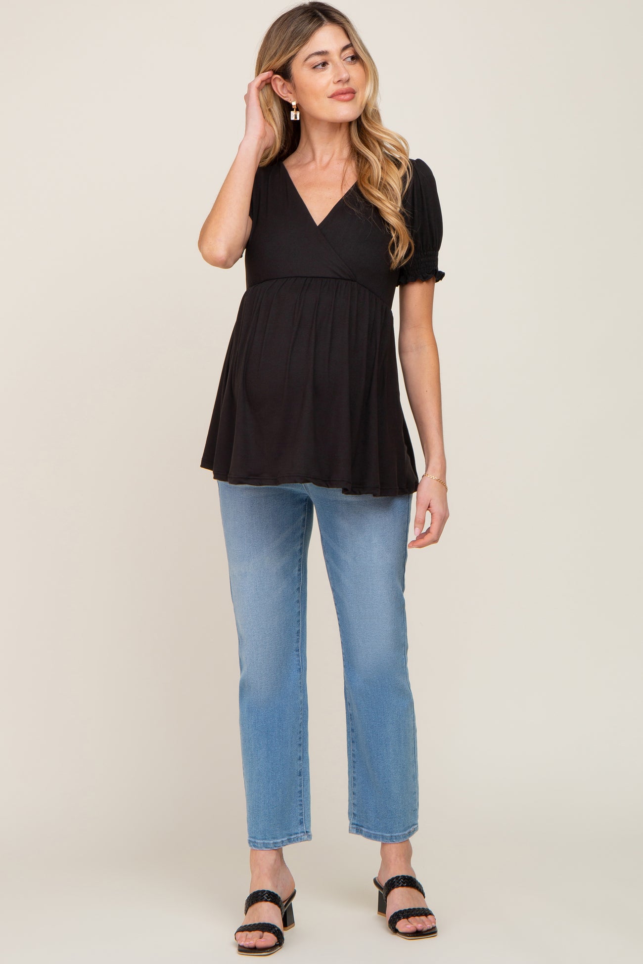 woman wearing a black maternity top with puff sleeves and a fitted waist paired with light blue jeans