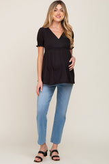 woman wearing a black short sleeve maternity top with a flared hem and blue jeans, showing her baby bump