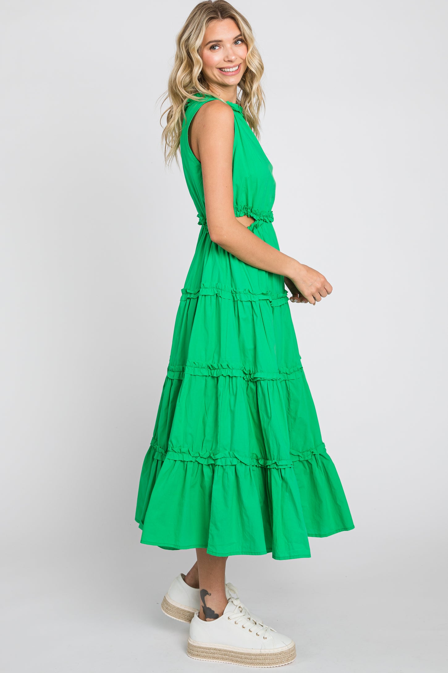 woman wearing a green tiered maxi dress with a fitted bodice and ruffled hem, smiling and posing sideways