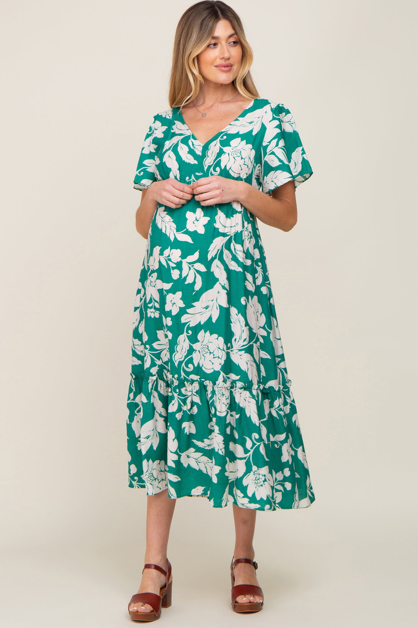 woman wearing a green floral print maternity dress with a tiered skirt and short sleeves, holding her baby bump