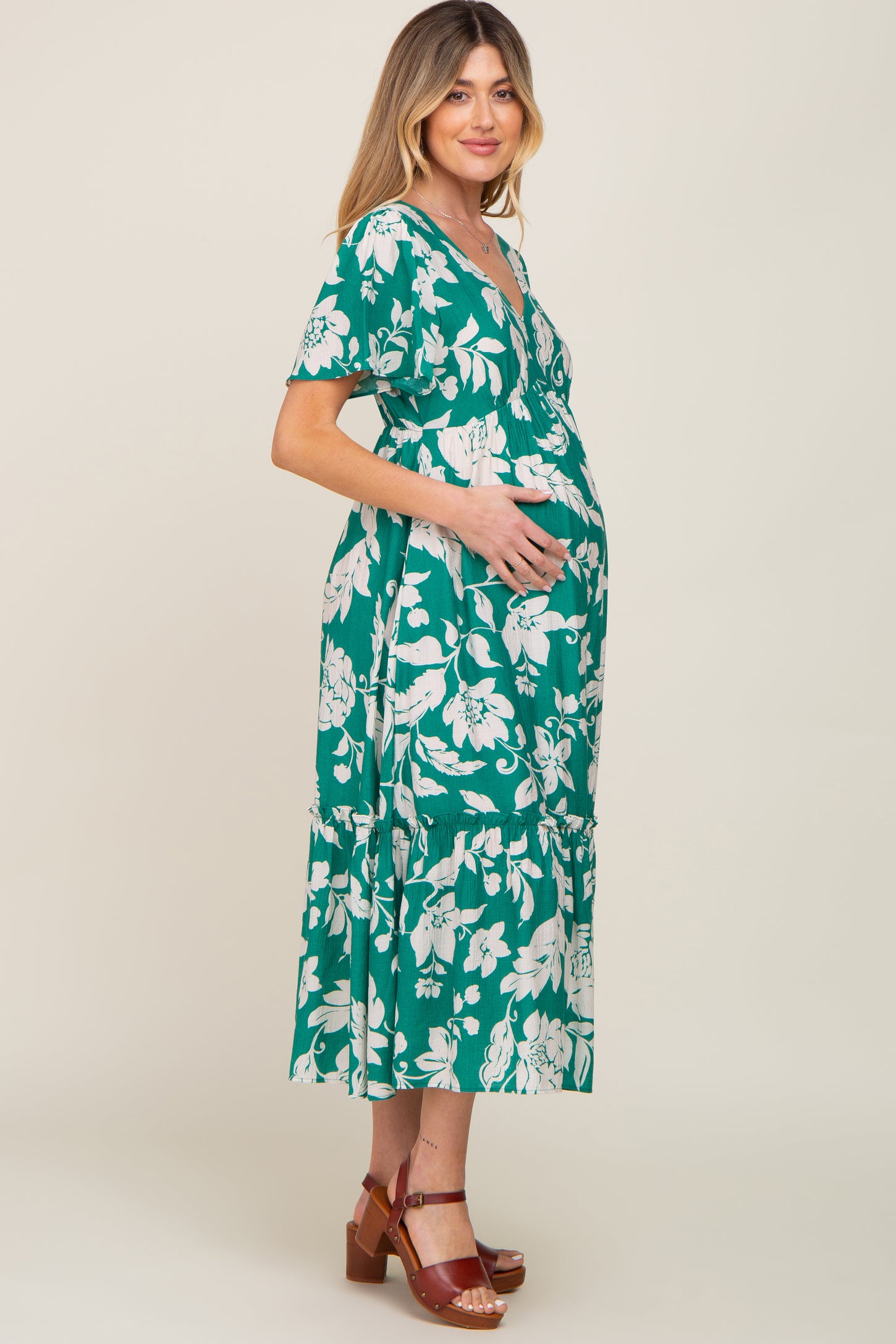 woman wearing a green floral print maternity dress and holding her baby bump