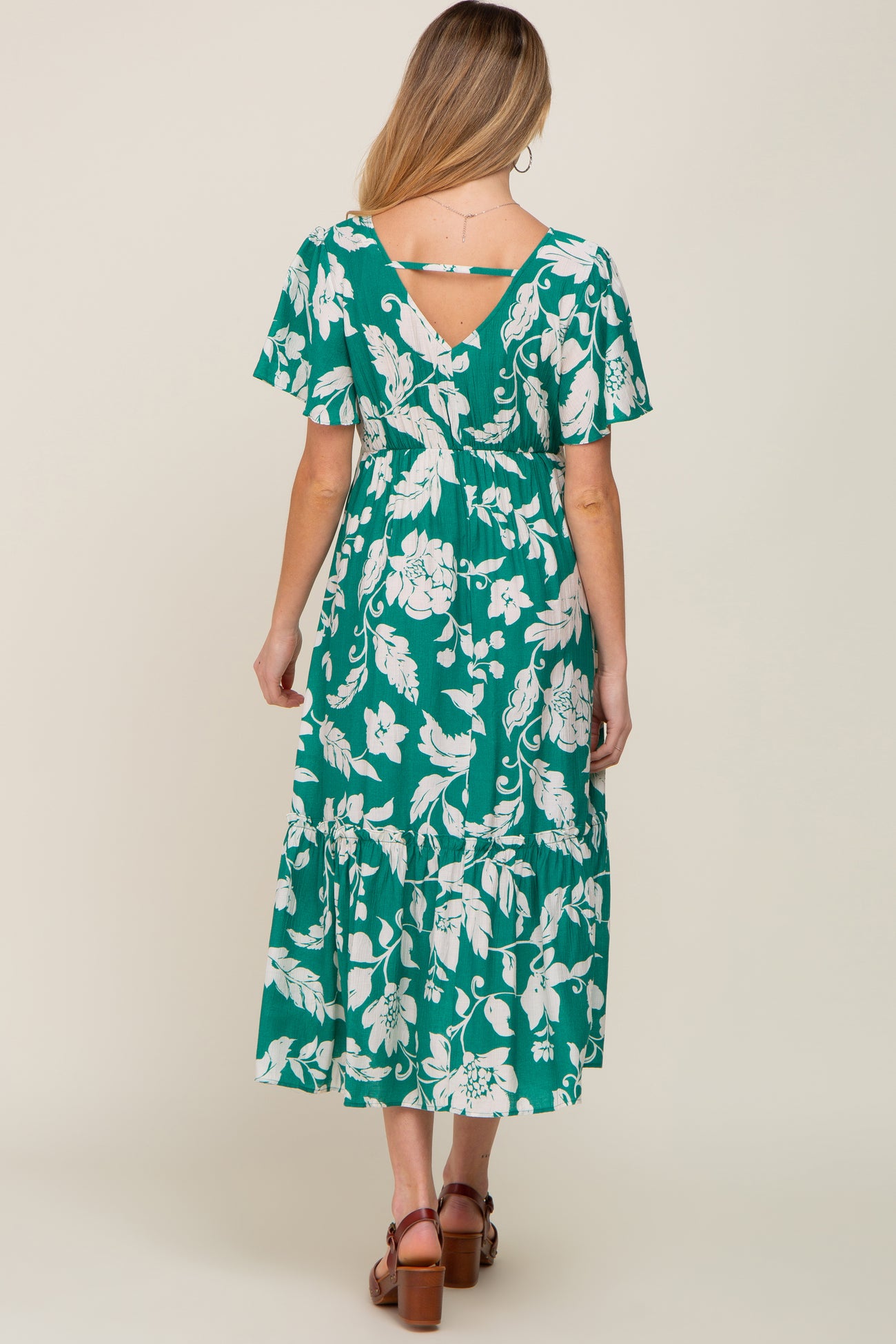 woman wearing a green floral maternity dress with short sleeves and a tiered skirt, showcasing her baby bump from the back