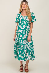 woman wearing a green floral maternity dress with short sleeves and tiered skirt, showcasing her baby bump
